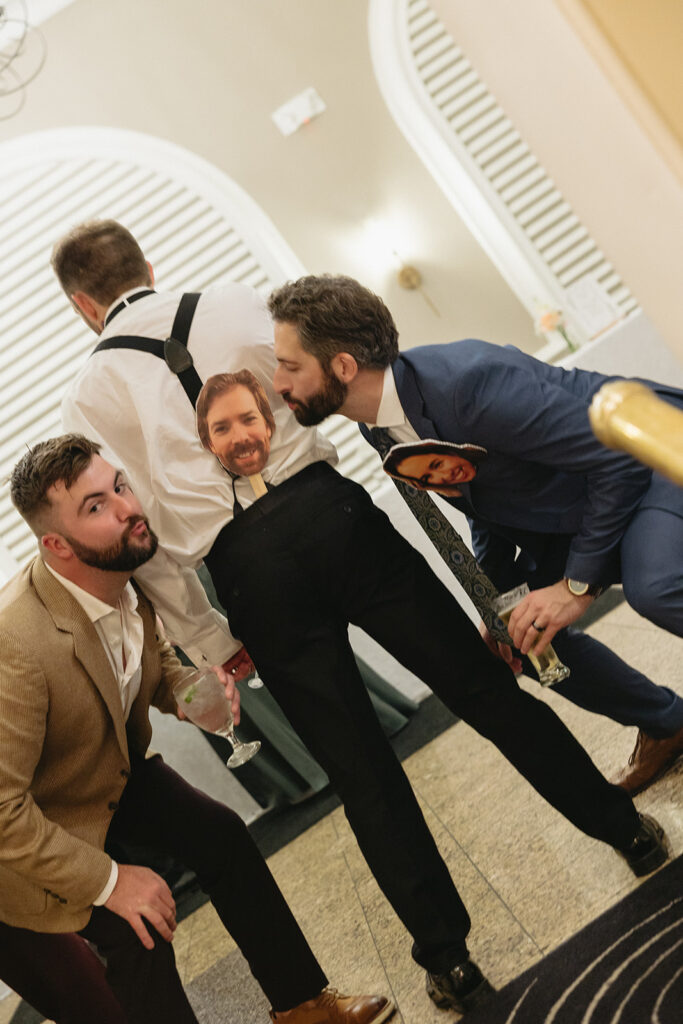 Groomsmen posing playfully with cutouts of the couple's faces at the Pine Knob Mansion wedding