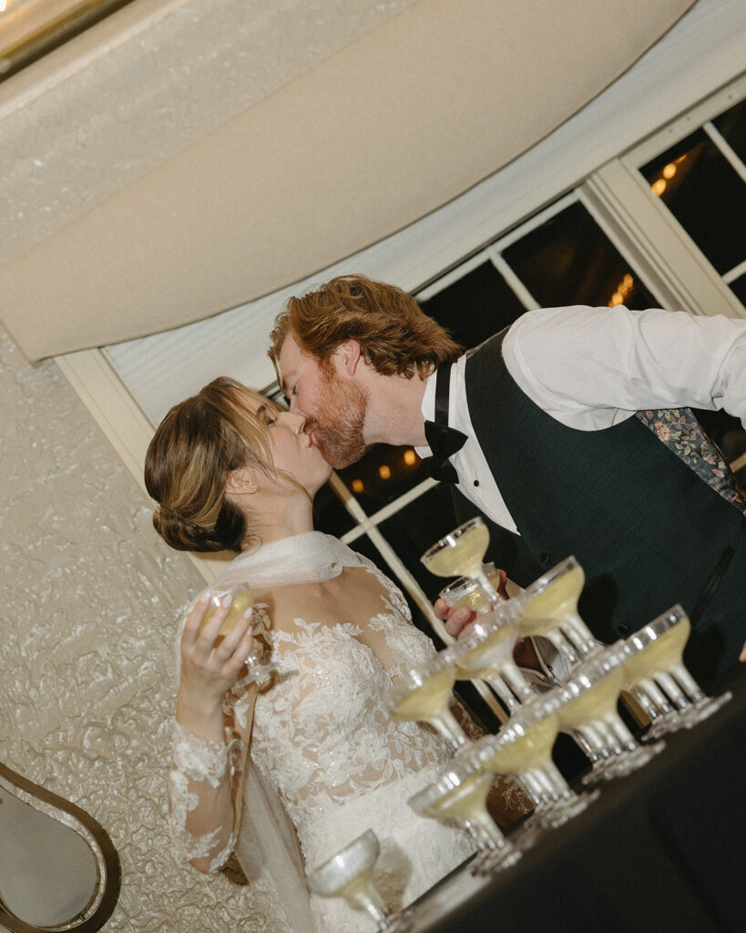 Bride and groom kissing in front of a champagne tower at their Pine Knob Mansion wedding
