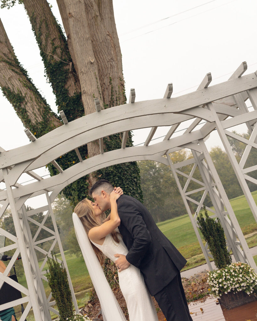 Bride and groom kissing during their rainy outdoor Fox Hill Golf Club wedding ceremony in greater Detroit
