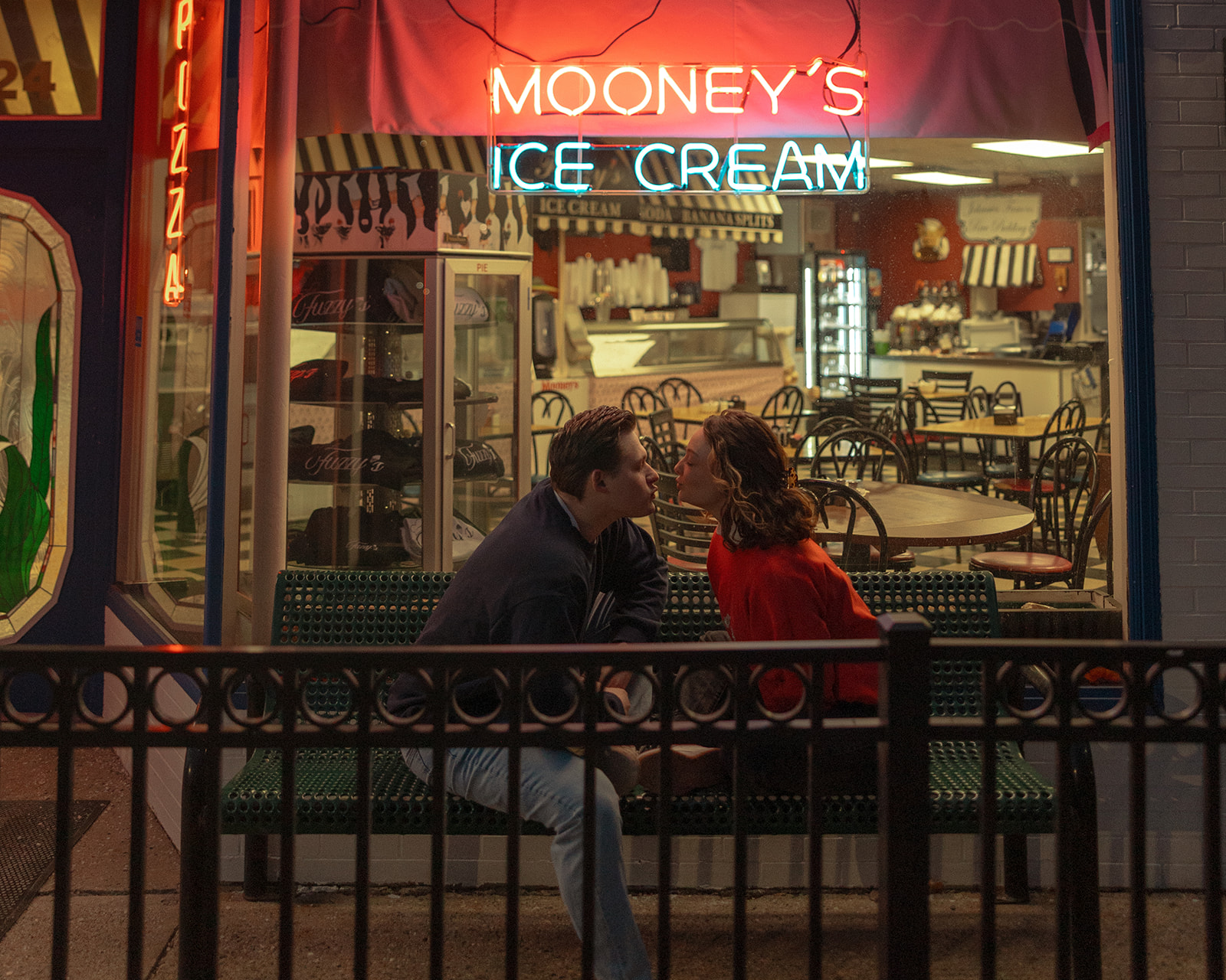 Couple sitting on a bench in front of Mooney's Ice Cream in Michigan for their engagement shoot
