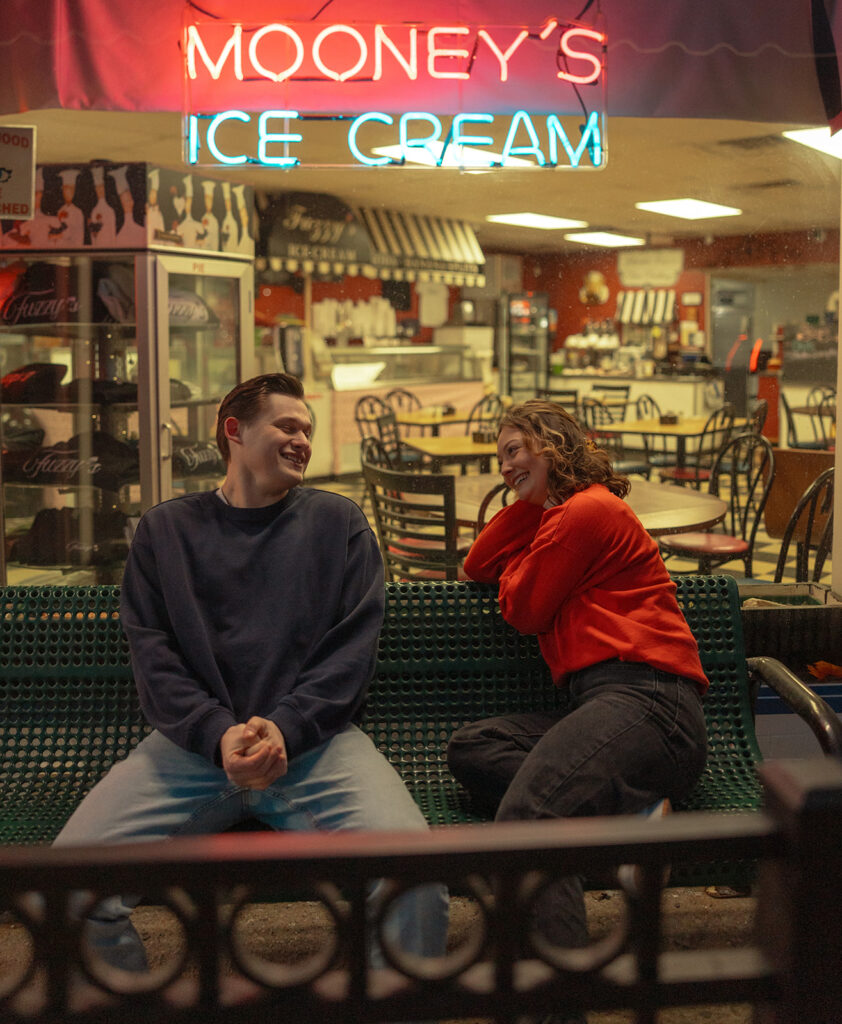 Man and woman laughing on a bench together outside of Mooney's Ice Cream in Michigan