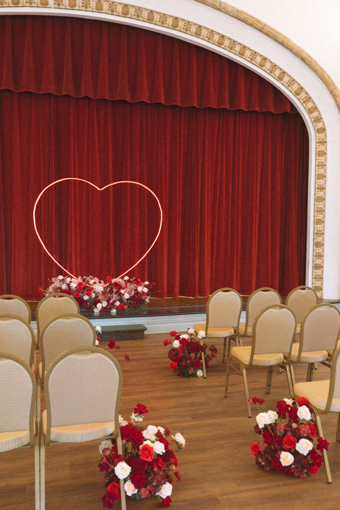 A bold heart-shaped neon light glows against a red velvet curtain at The Lit in Grand Rapids, Michigan