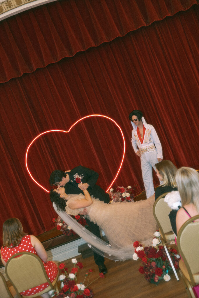 Liv and Dylan share a dramatic dip-and-kiss moment on stage while Elvis officiates their ceremony