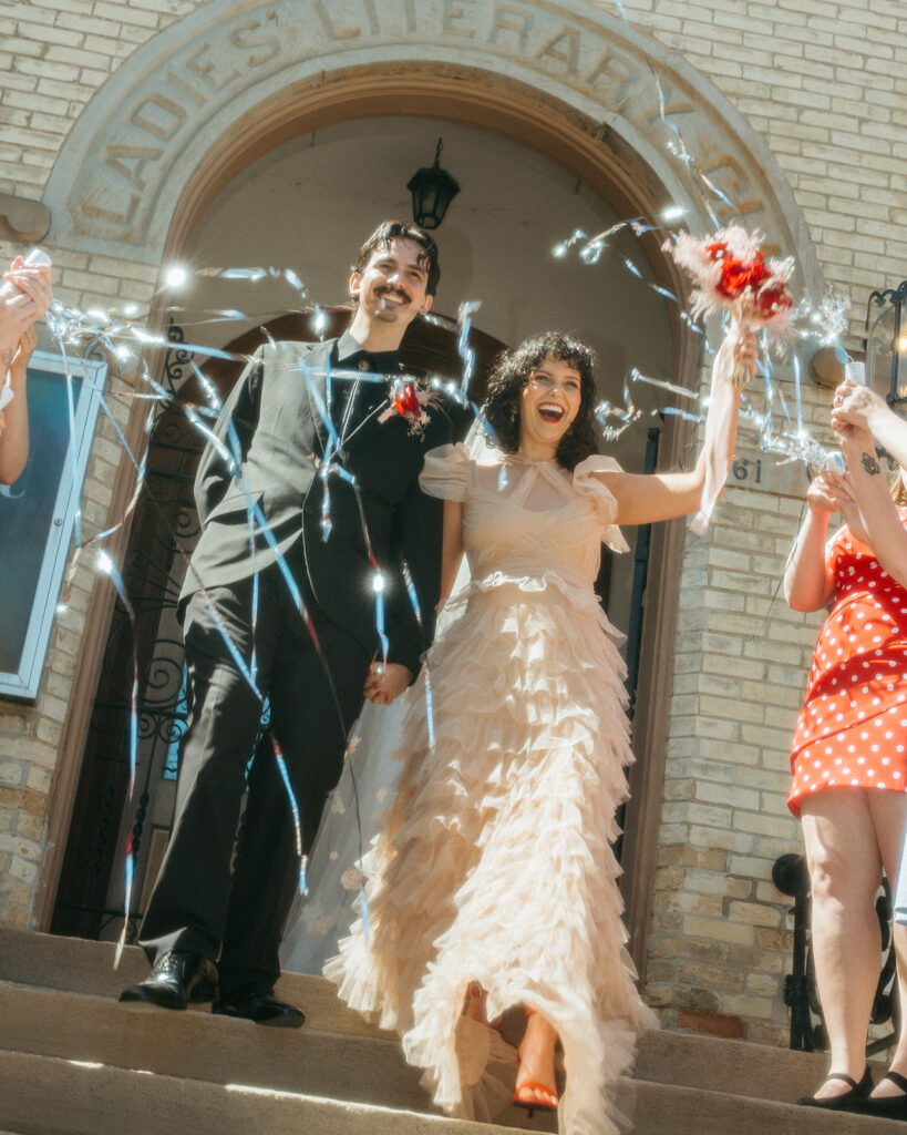 Newlyweds exit the Ladies Literary Club in downtown Grand Rapids under a flurry of metallic streamers, celebrating their Michigan elopement in style.