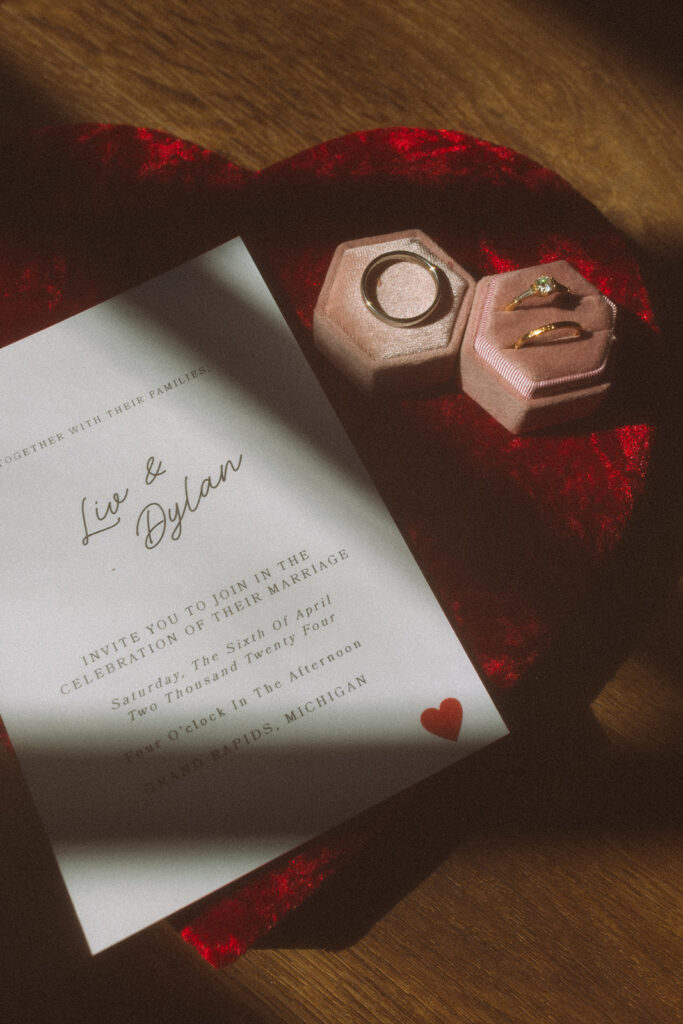 Artistic flatlay of wedding rings in velvet hexagonal boxes, paired with a wax-sealed envelope and vintage red velvet heart box.