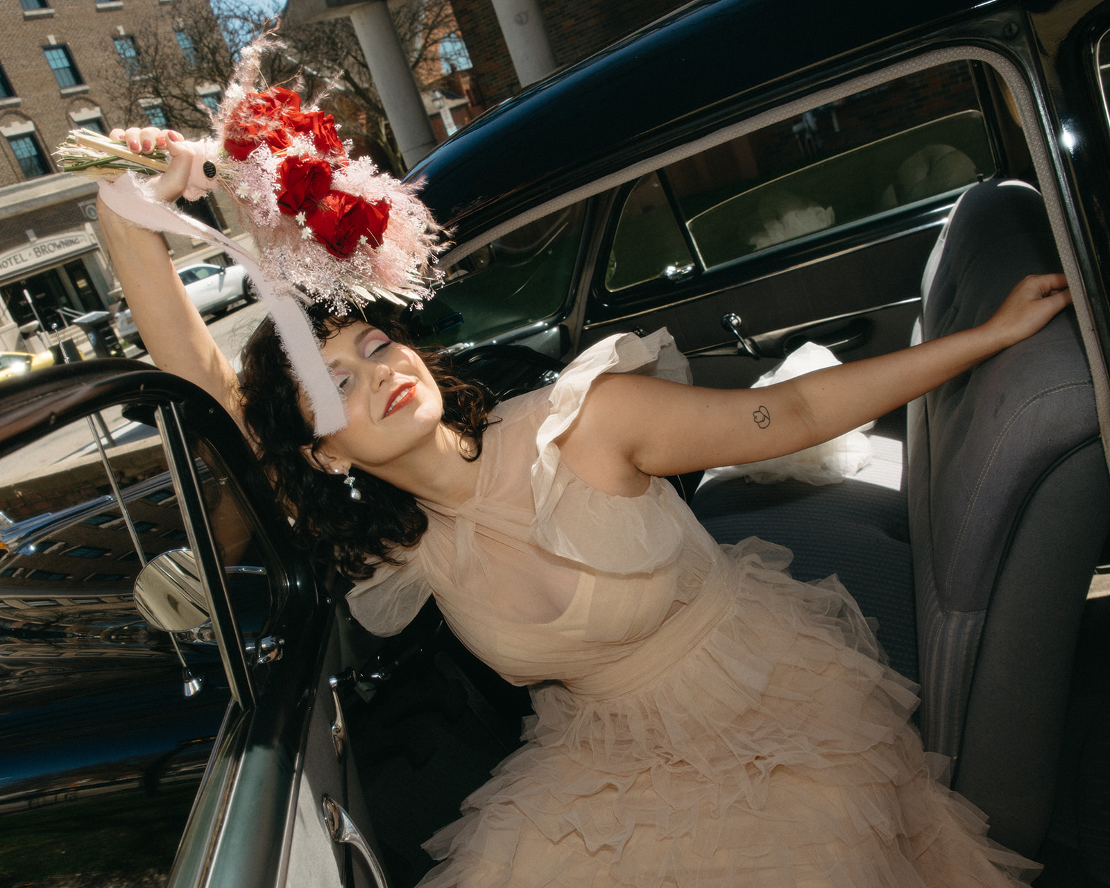 Bride holding bouquet while seated in vintage car on downtown Michigan street.