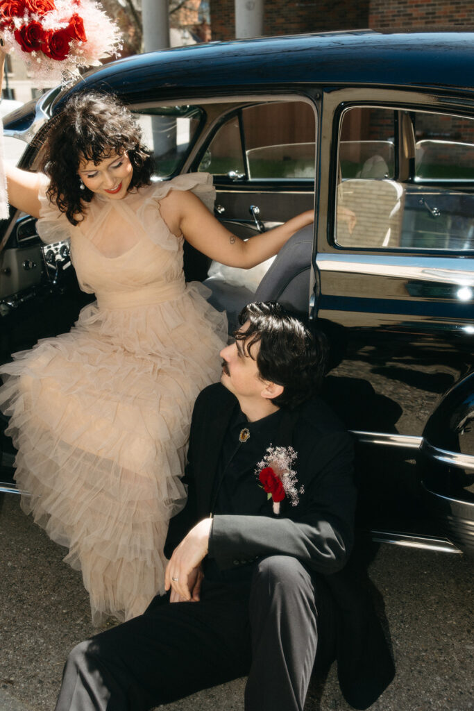 Bride and groom posing with vintage black car during stylish Michigan elopement
