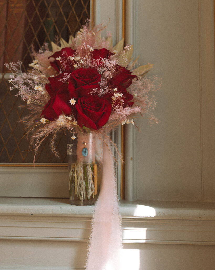 Moody bouquet shot featuring red roses, blush-toned florals, and soft ribbon details arranged in a vintage Coca-Cola glass bottle.