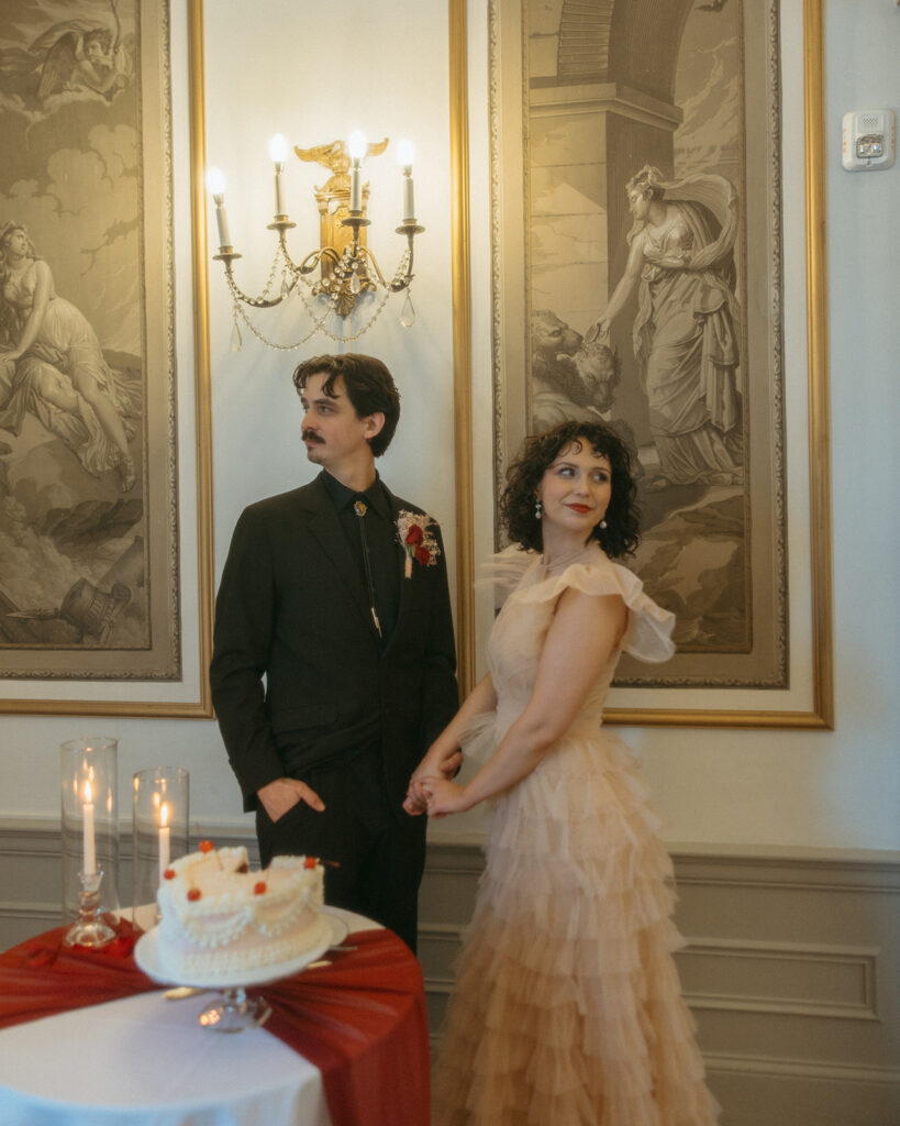 Bride and groom posing next to their elopement cake