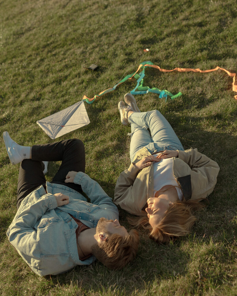 Couple laying in the grass after flying kites for their Michigan engagement photos