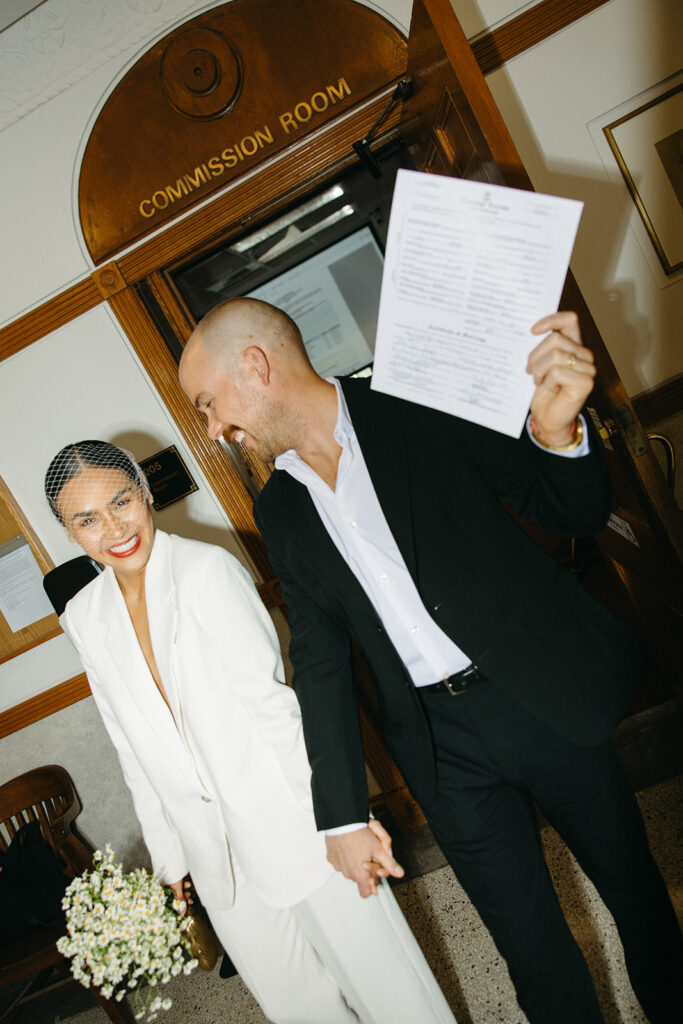 Newlyweds celebrating outside the Commission Room holding their marriage license at City Hall.