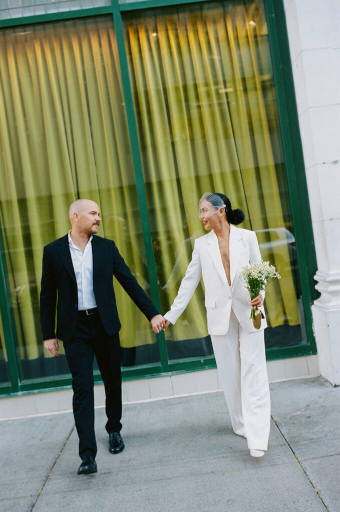 Couple holding hands in front of a green backdrop window captured on film. 