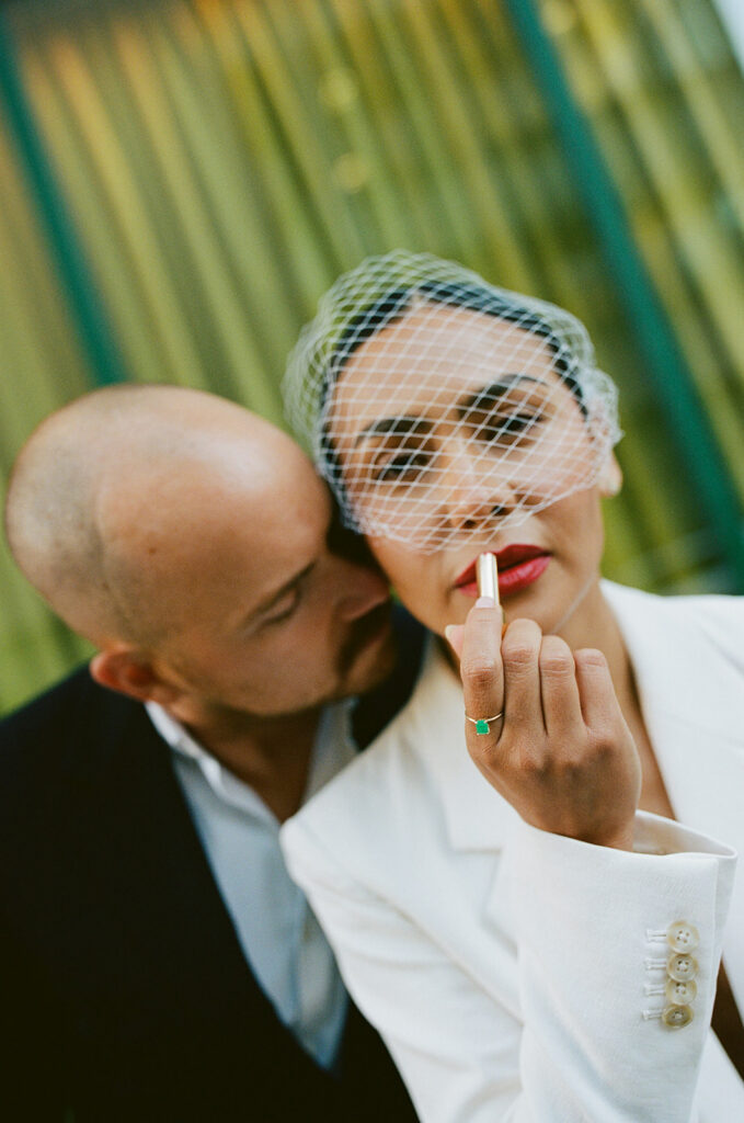 Film photo of a bride applying lipstick next to the groom.