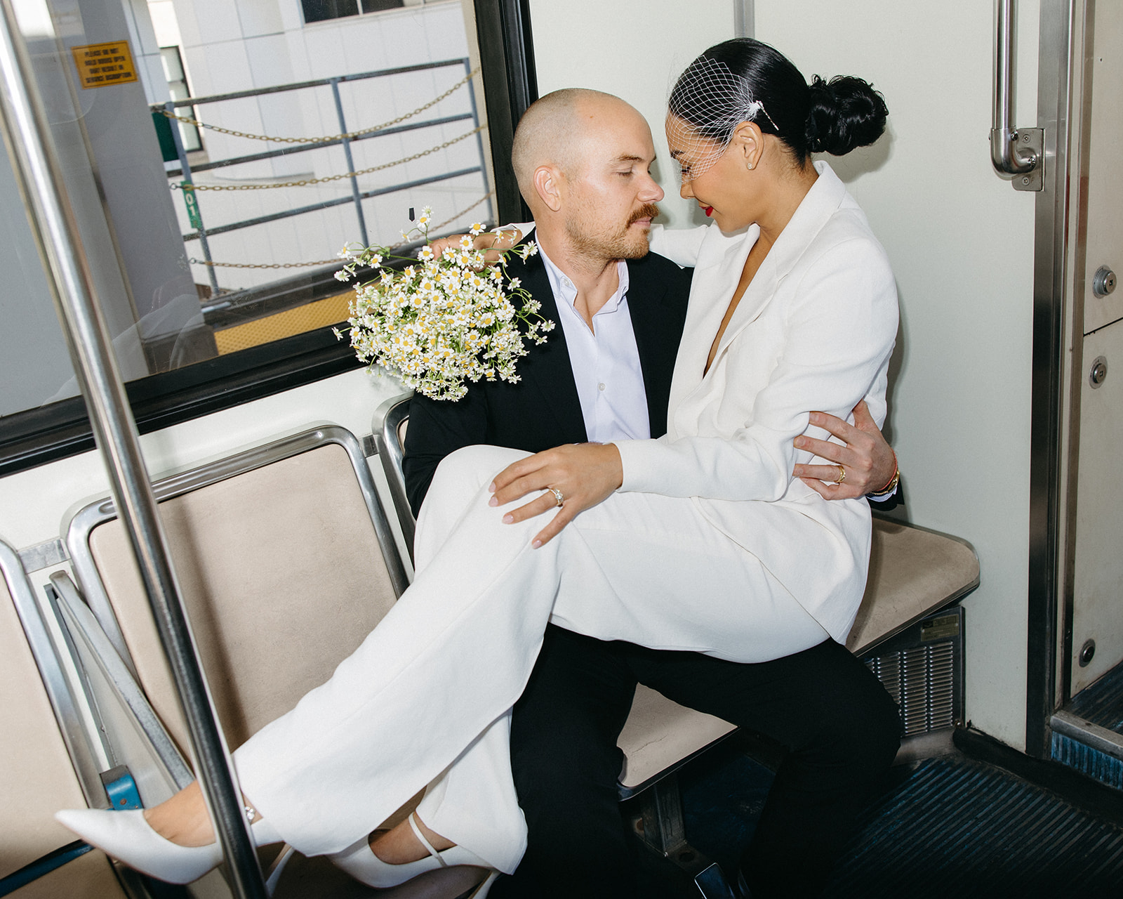 Bride sitting on groom’s lap holding a daisy bouquet inside the Detroit People Mover.