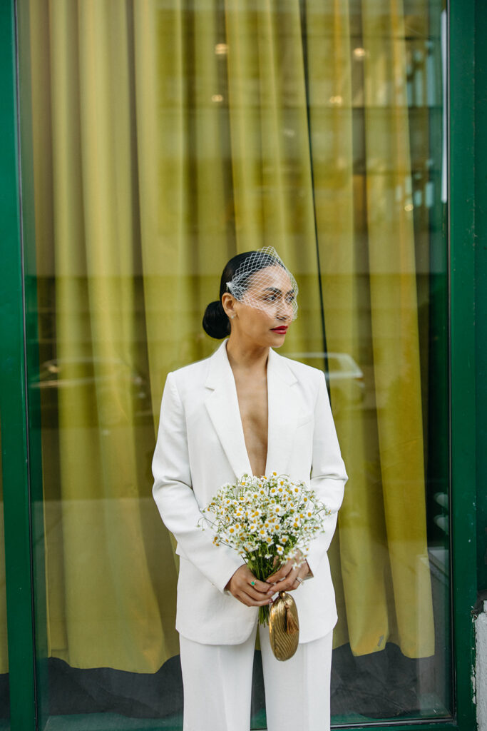 Portrait of bride in ivory suit and birdcage veil holding daisy bouquet during Detroit elopement.