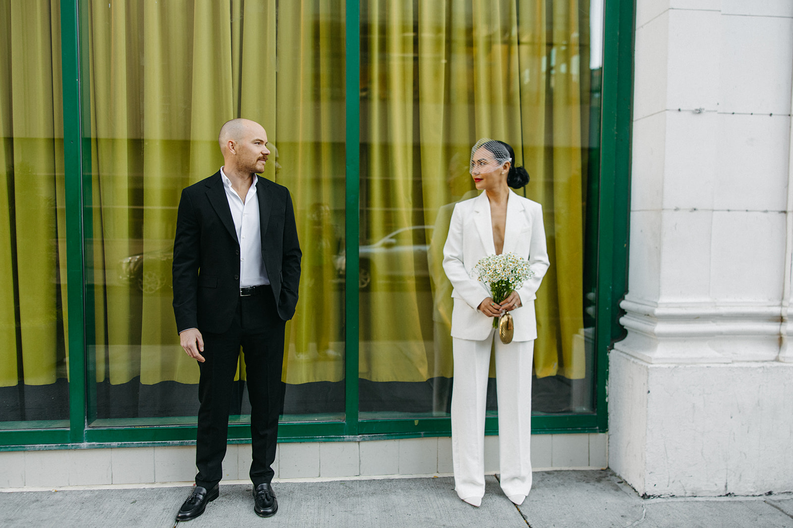 Wide shot of a bride and groom posing in front of a green window backdrop in downtown Detroit for their elopement photos. 