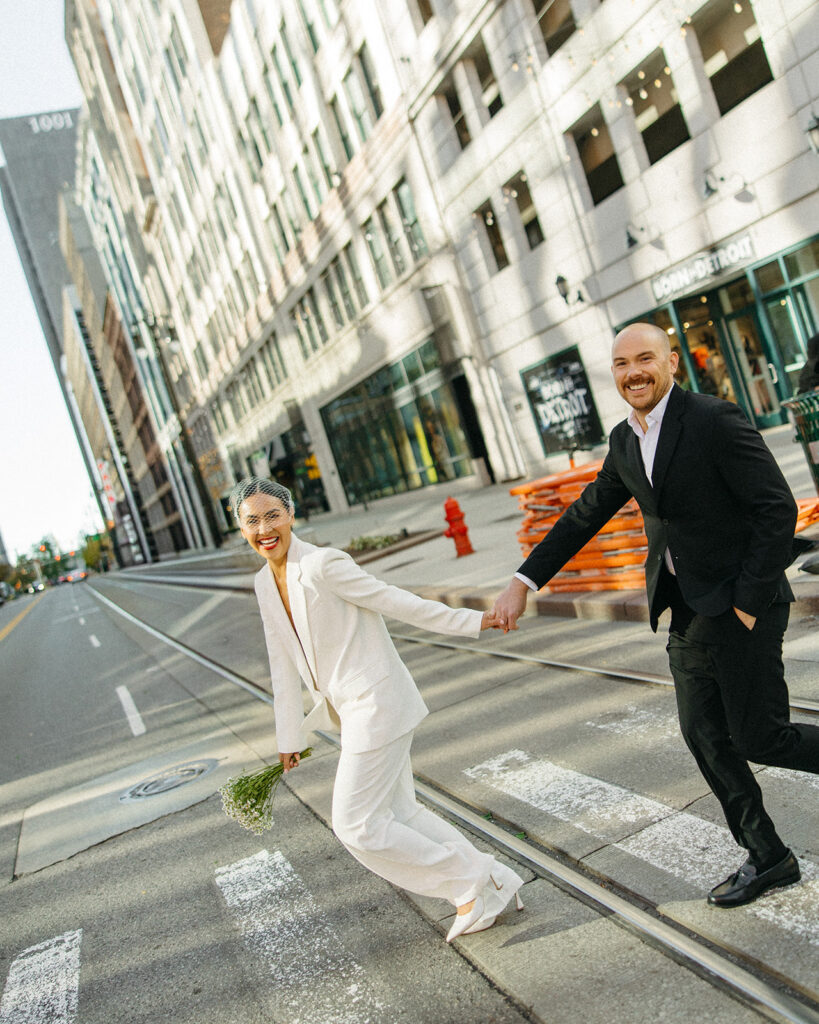 Couple holding hands and running across the street for their downtown Detroit elopement photos. 
