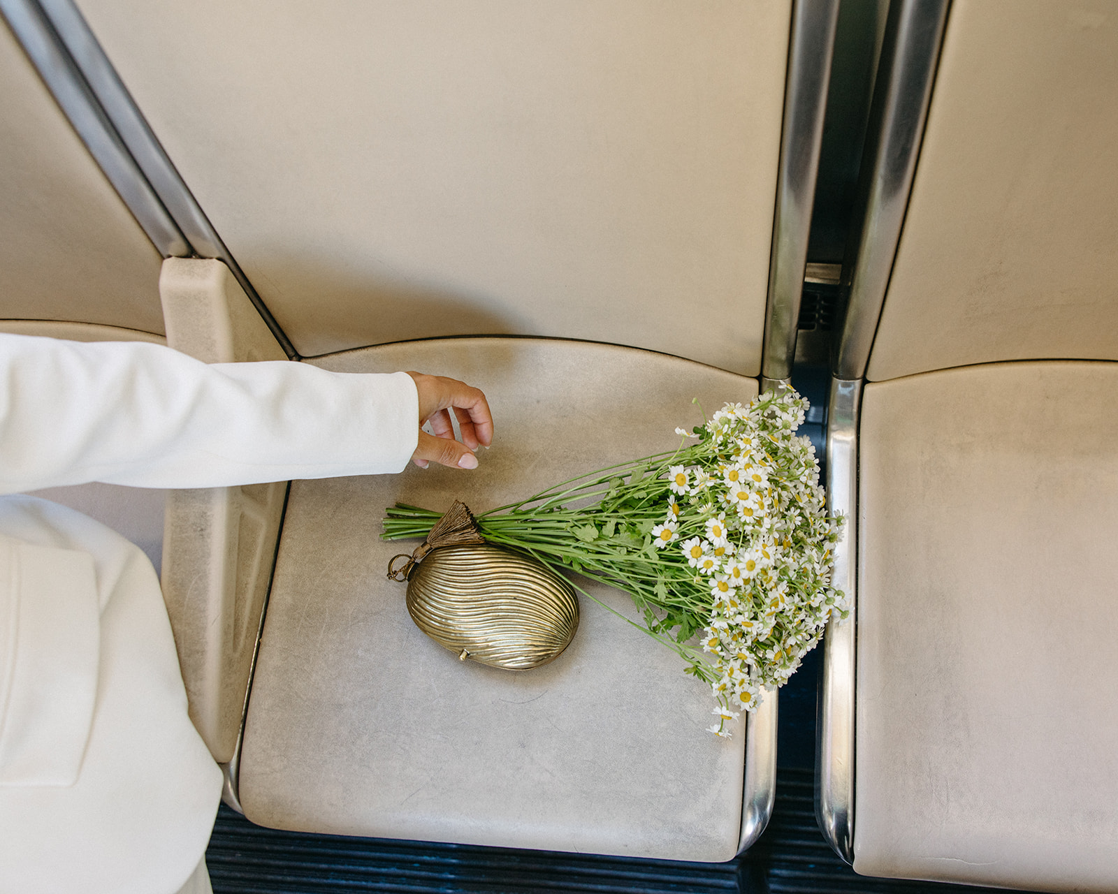 Bride’s gold clutch and daisy bouquet resting on a People Mover seat during a Detroit elopement.