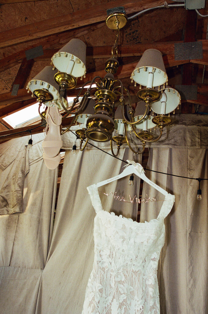Film wedding details of a dress and heels hanging from a chandelier. 