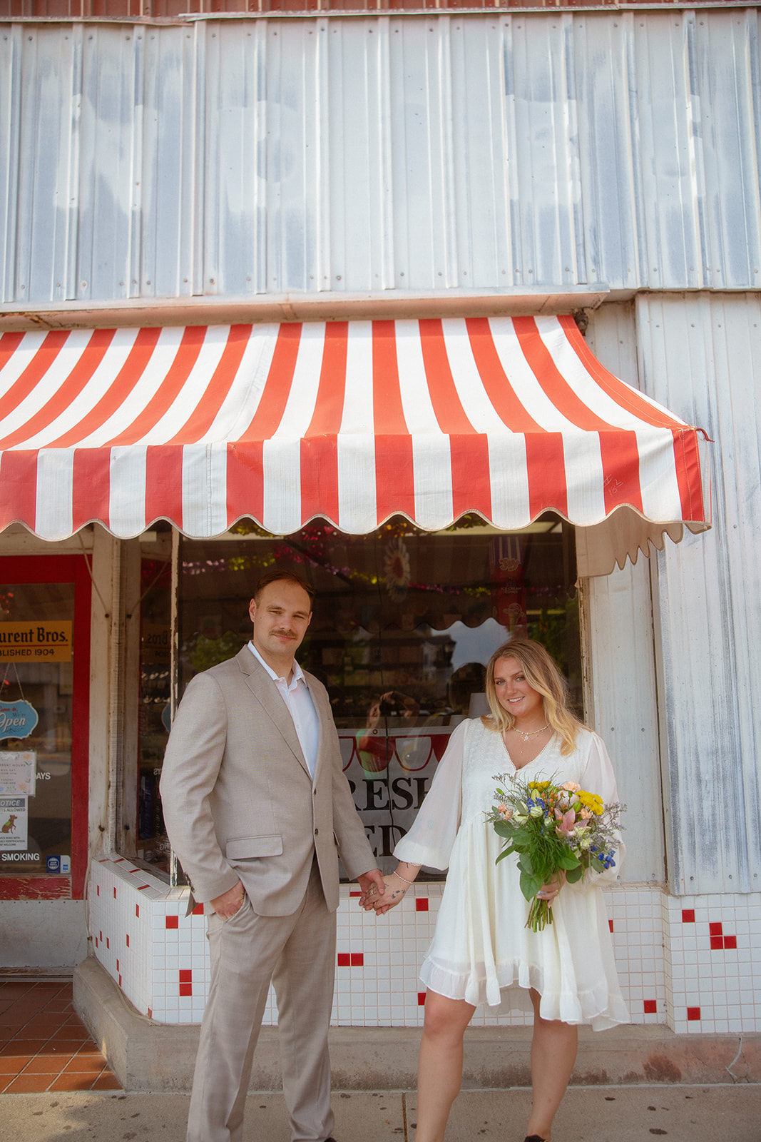 Bride and groom holding hands in front of a Bay City store after their Michigan elopement.