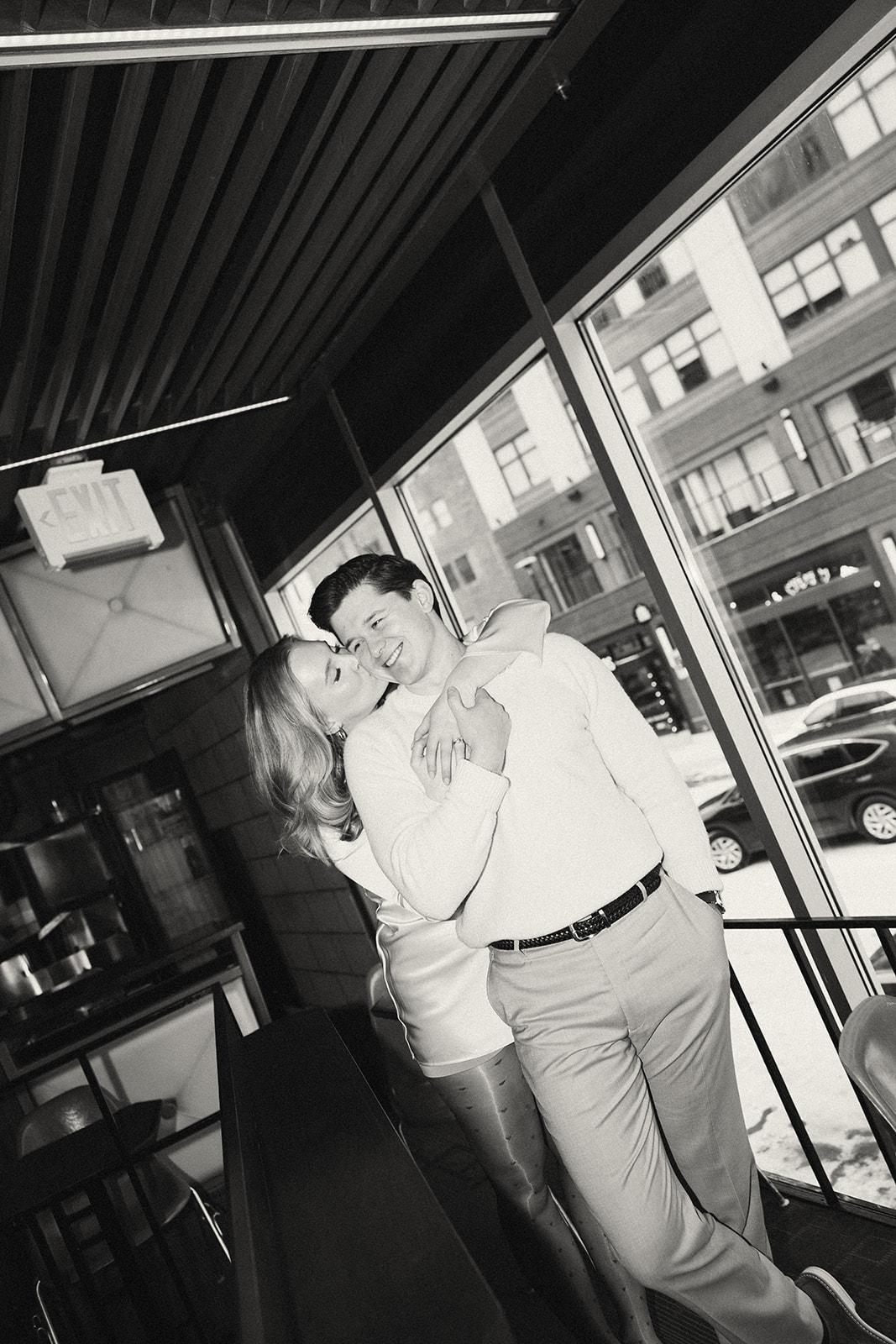 Black and white photo of woman kissing her fiancé on the cheek during Detroit engagement photos at SPKRBOX.