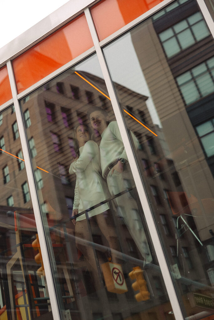 Exterior view of SPKRBOX in downtown Detroit with couple visible through window during Detroit engagement photos.