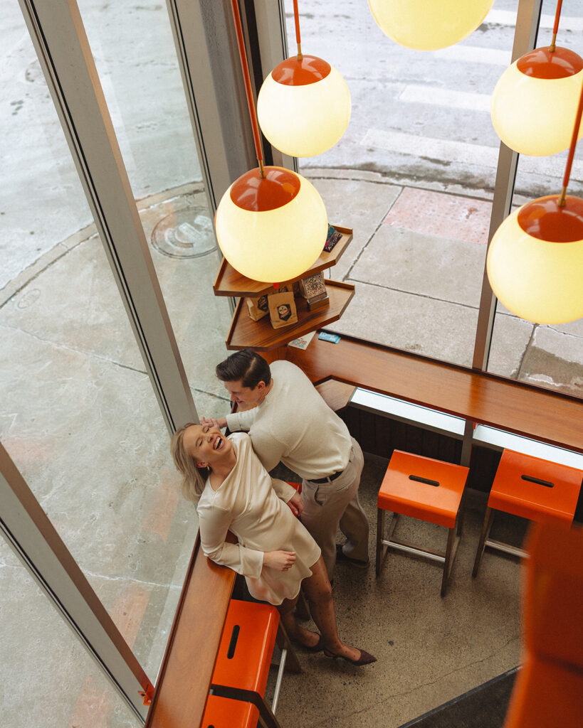 Overhead photo of couple laughing together near window seating during Detroit engagement photos at SPKRBOX.