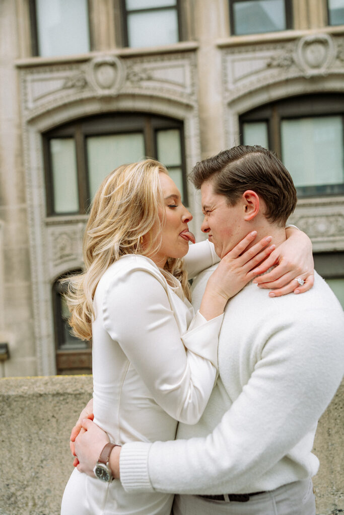 Woman sticking her tongue out at her fiancés during their photoshoot on a rooftop.