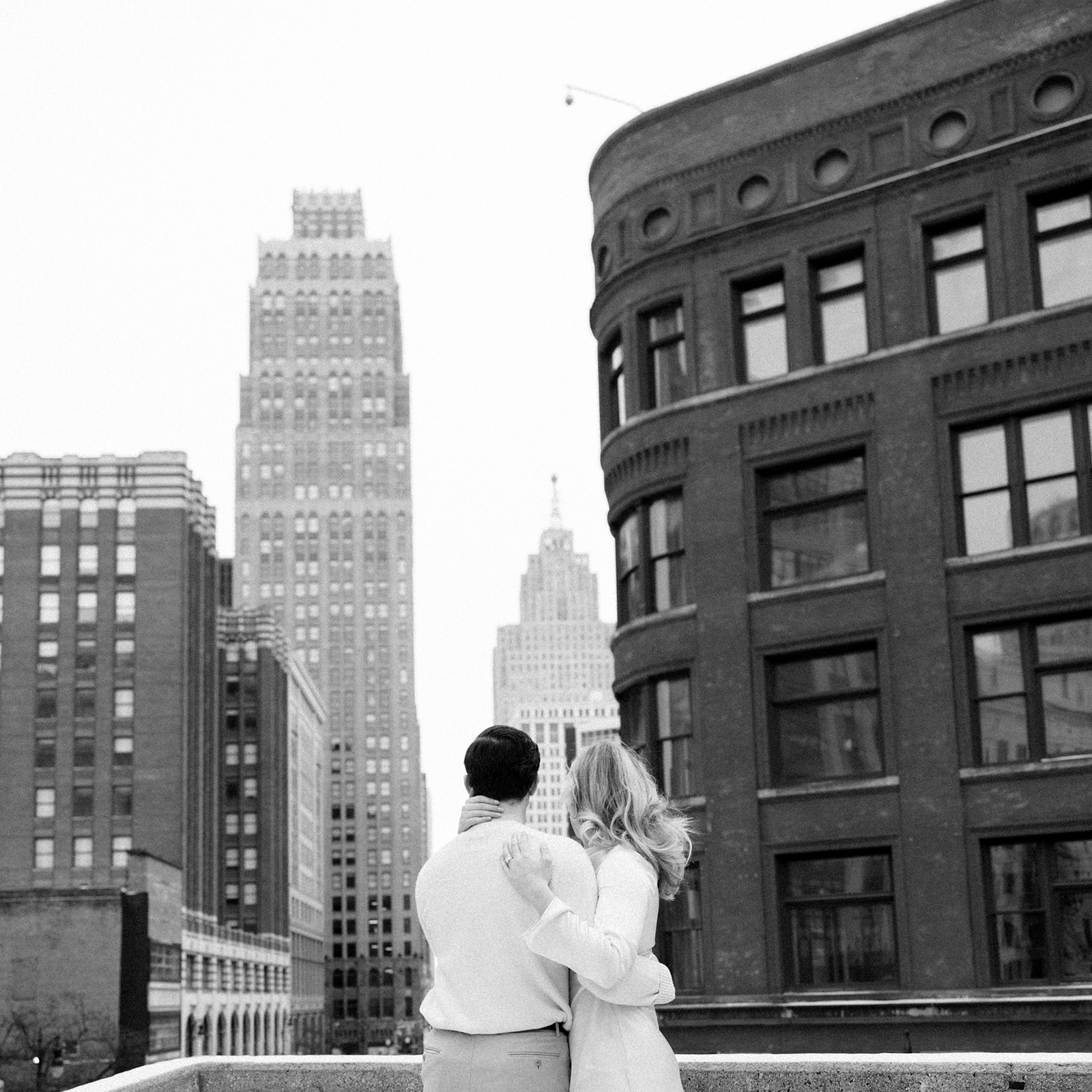 Black and white photo of a couple overlooking the downtown Detroit skyline rooftop engagement photo.