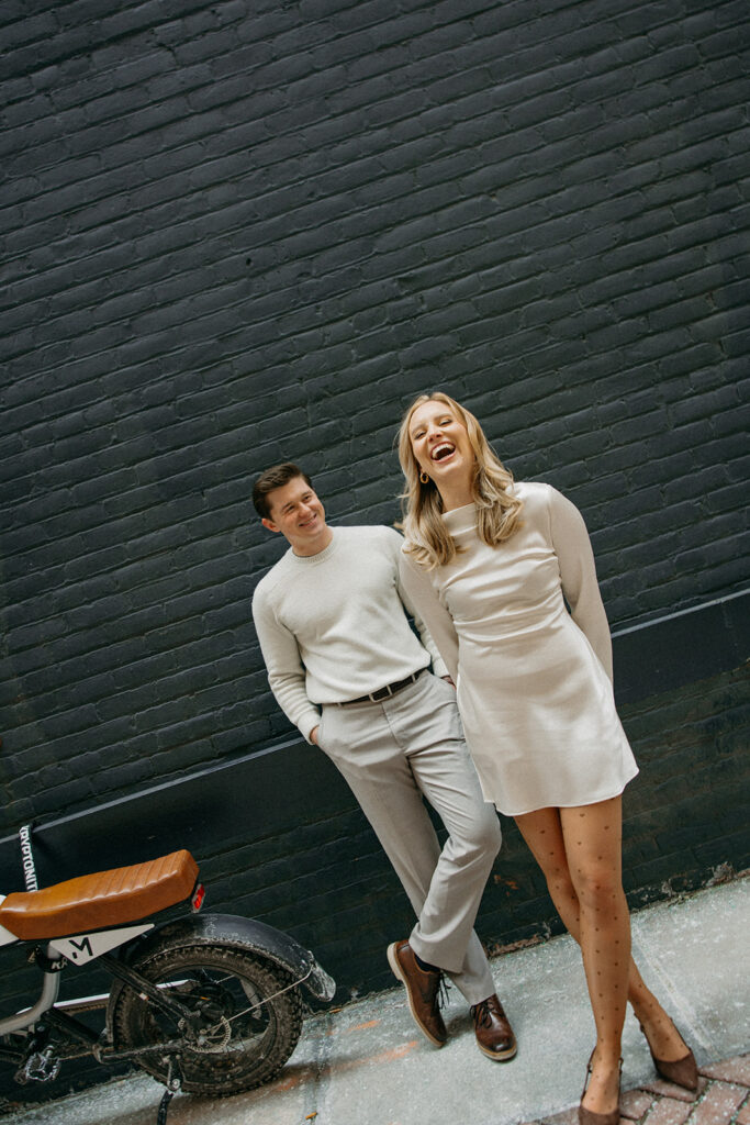 Candid photo of a couple laughing next to a motorcycle in a downtown Detroit alleyway.