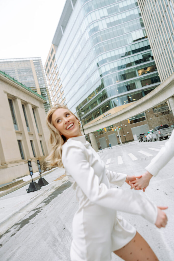 Couple holding hands and running across a street in downtown Detroit.