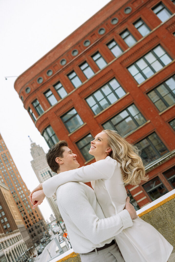 Candid engagement photo of a couple posing on a rooftop in Detroit during the winter.