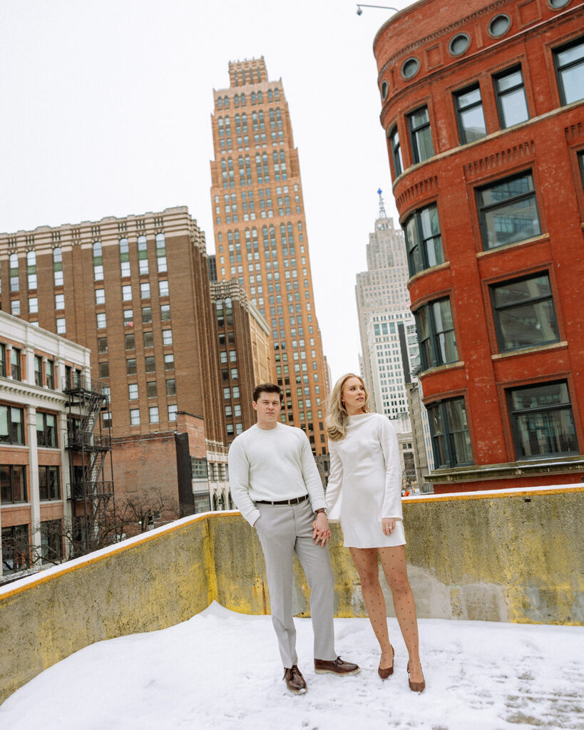 Couple holding hands and posing on a rooftop during their winter Detroit engagement photos downtown.