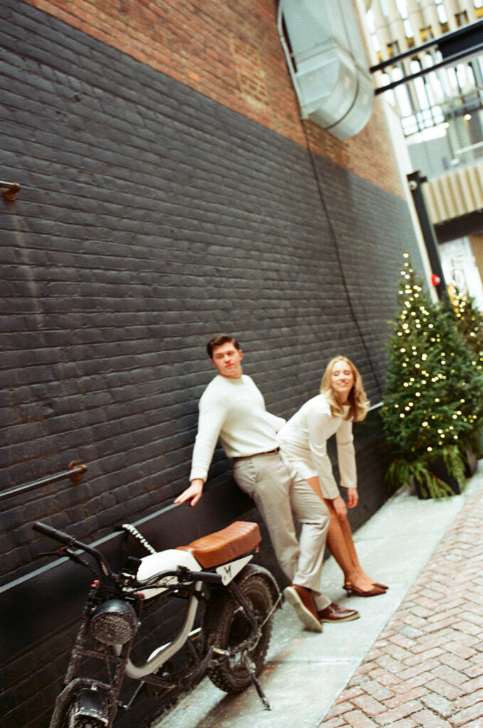 Couple leaning against a wall next to a motorcycle in a Detroit alley, captured on 35mm film.
