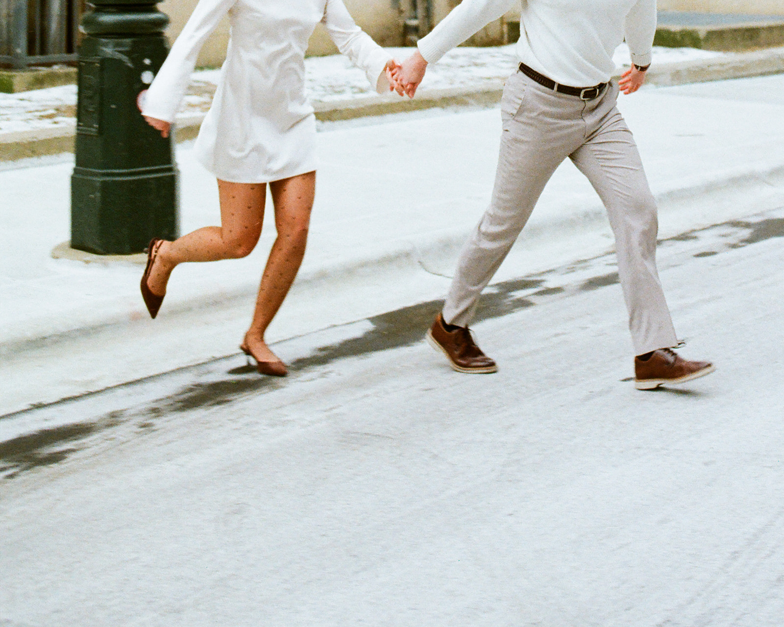 Couple running hand in hand through a snowy downtown Detroit street, captured on film.