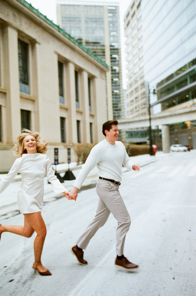 Couple running hand in hand through downtown Detroit street, captured on film.