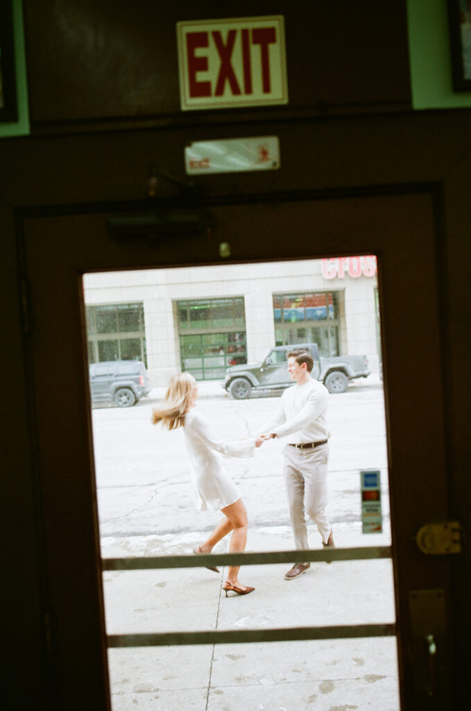 Documentary style engagement photo of a couple dancing outside of a business door in downtown Detroit.