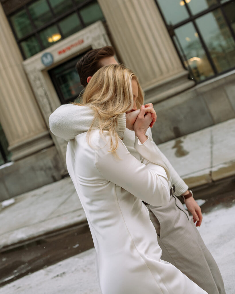 Couple walking arm in arm past downtown Detroit buildings during their engagement session.