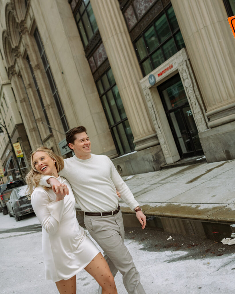 Couple walking past downtown Detroit buildings during their engagement session.