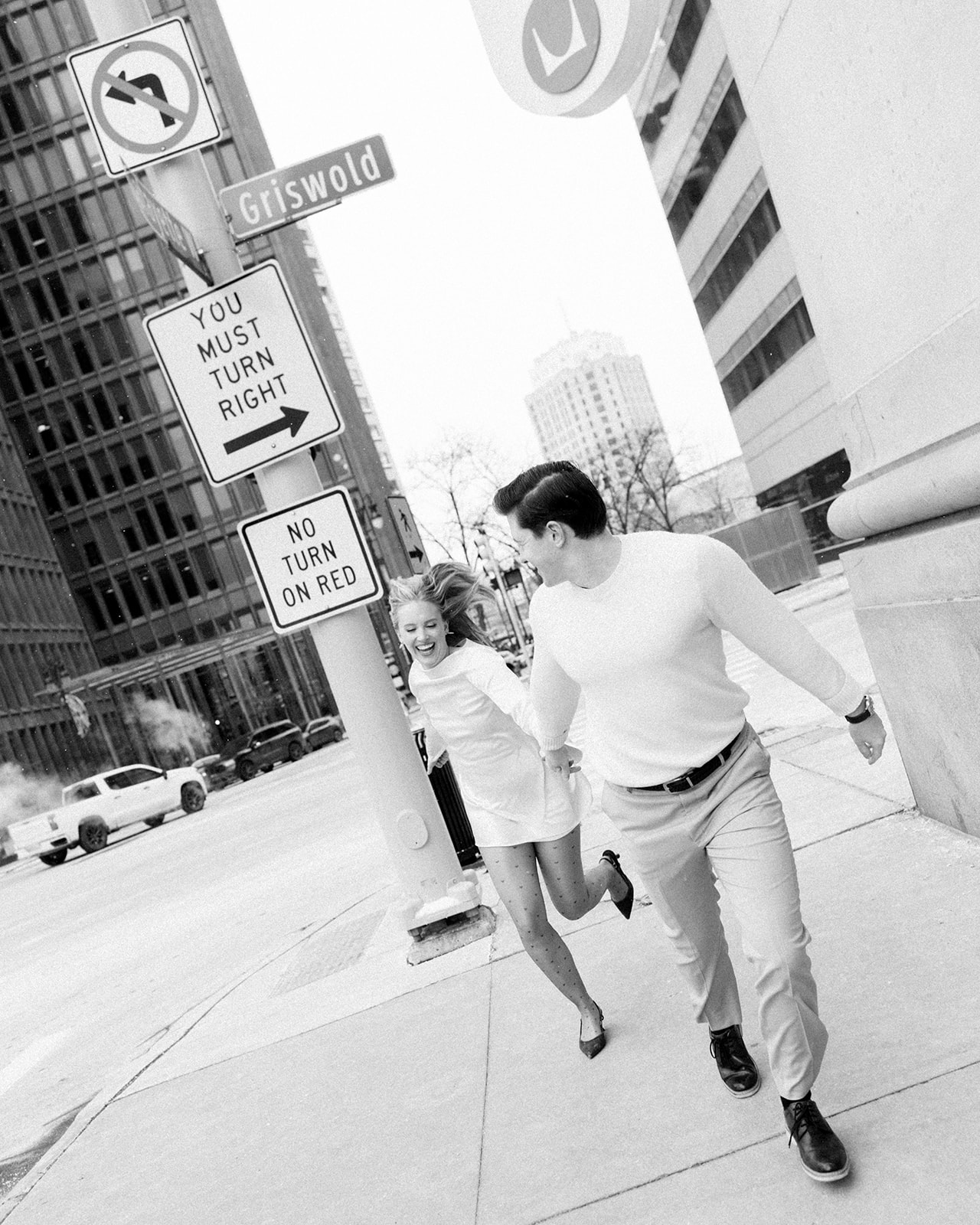 Black and white photo of couple running together on a downtown Detroit sidewalk.
