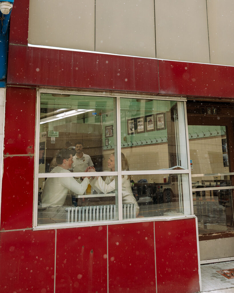 Exterior view of couple sitting inside Lafayette Coney Island through the front window in Detroit.