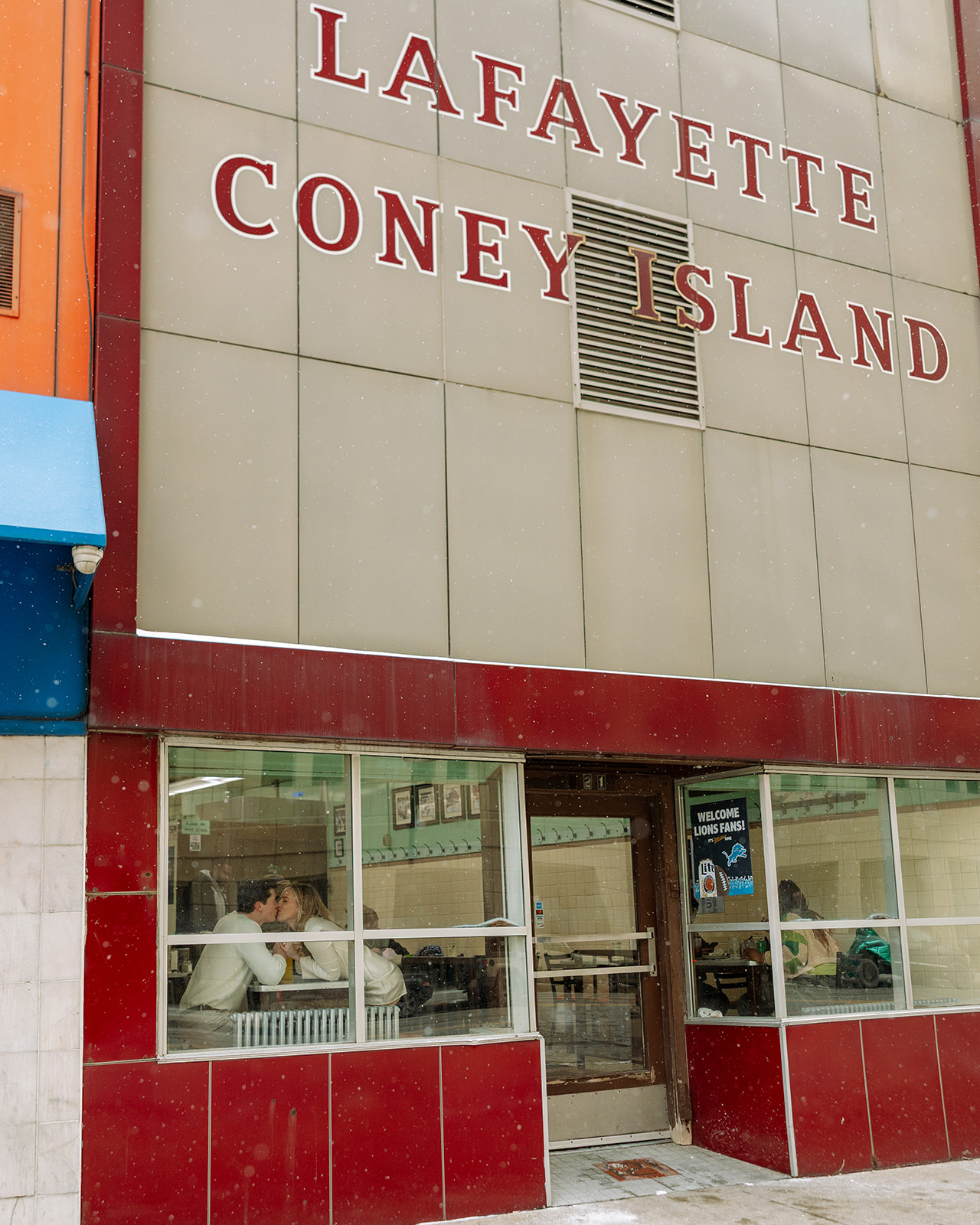 Documentary style engagement photo of a couple kissing through the window inside of Lafayette Coney Island in Detroit.