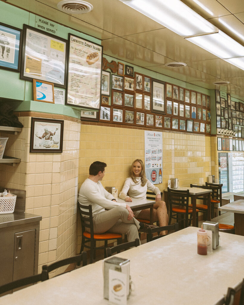 Couple sitting together at a table inside Lafayette Coney Island surrounded by tiled walls and framed photos.