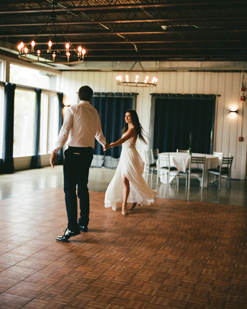 Bride and groom holding hands and dancing together on an empty reception dance floor before guests arrive.