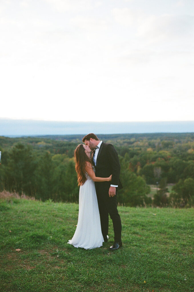 Bride and groom kissing at sunset overlooking hills during documentary wedding near Grand Rapids Michigan on film.