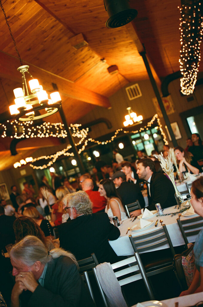 Wedding guests gathered for dinner with warm string lights at intimate Michigan reception on film.