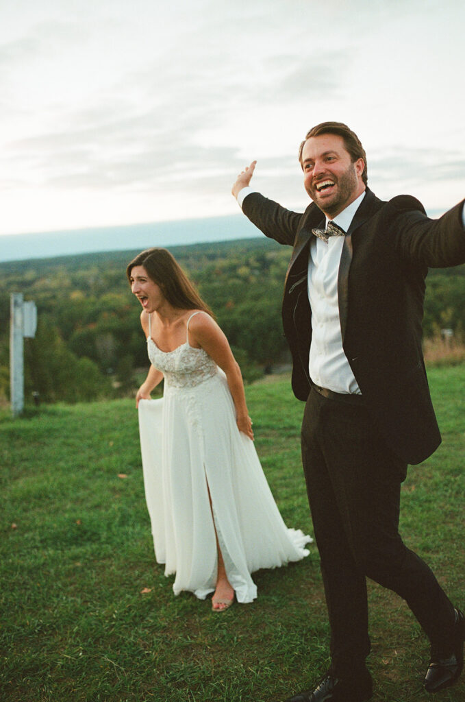 Bride and groom laughing together on hilltop during candid sunset moment at Michigan wedding on film.