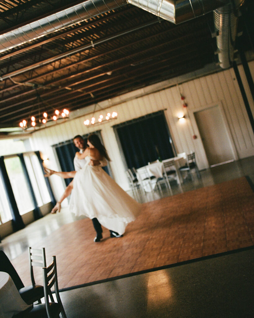 Groom lifting bride during a playful first dance on a quiet indoor dance floor.