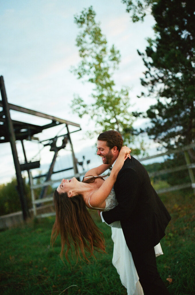 Bride and groom embracing and laughing together in unposed documentary wedding moment outdoors on film.