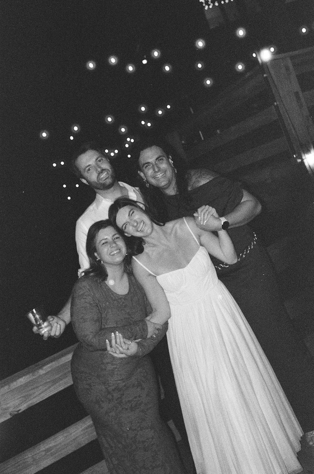 Couple posing with friends at night under string lights during candid wedding celebration on film.